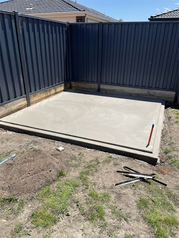 New concrete slab in a fenced backyard corner beside the lawn