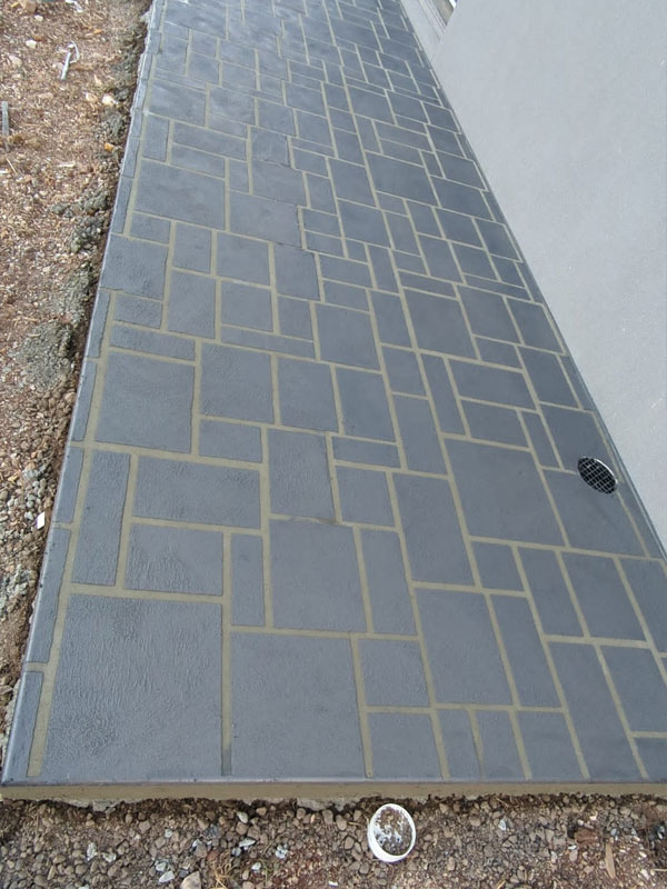 Charcoal paver-pattern stencilled concrete path along a light grey wall