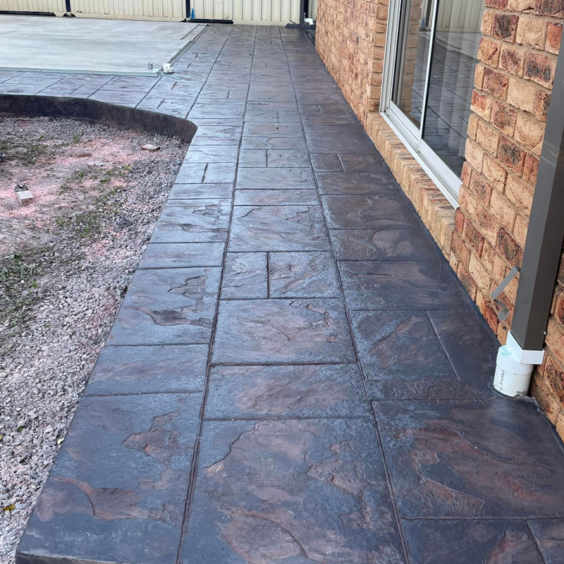 Grey stencilled concrete path curving beside a brick house