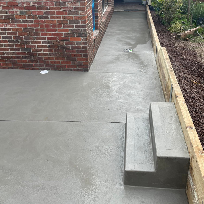 Freshly finished concrete path with steps beside a brick house