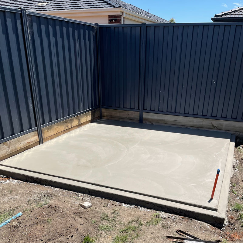 Smooth new concrete slab in a fenced backyard corner