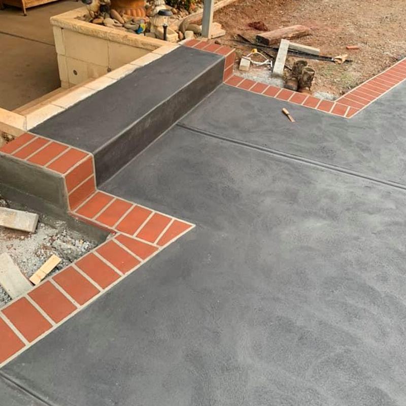 Grey concrete patio and step edged with red brick pavers