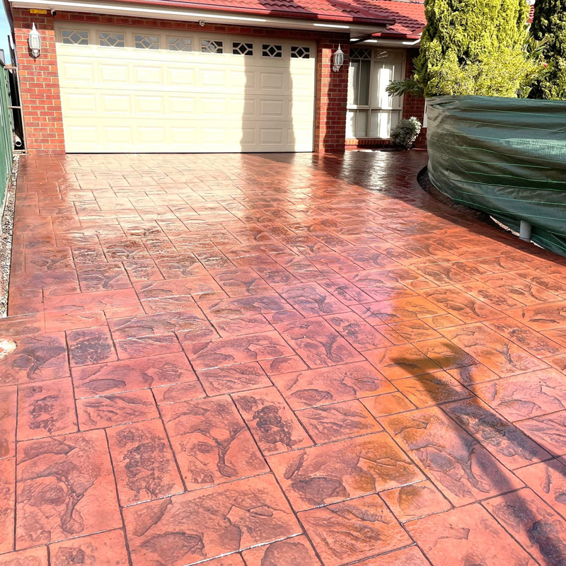 Glossy red stencilled concrete driveway leading to a garage