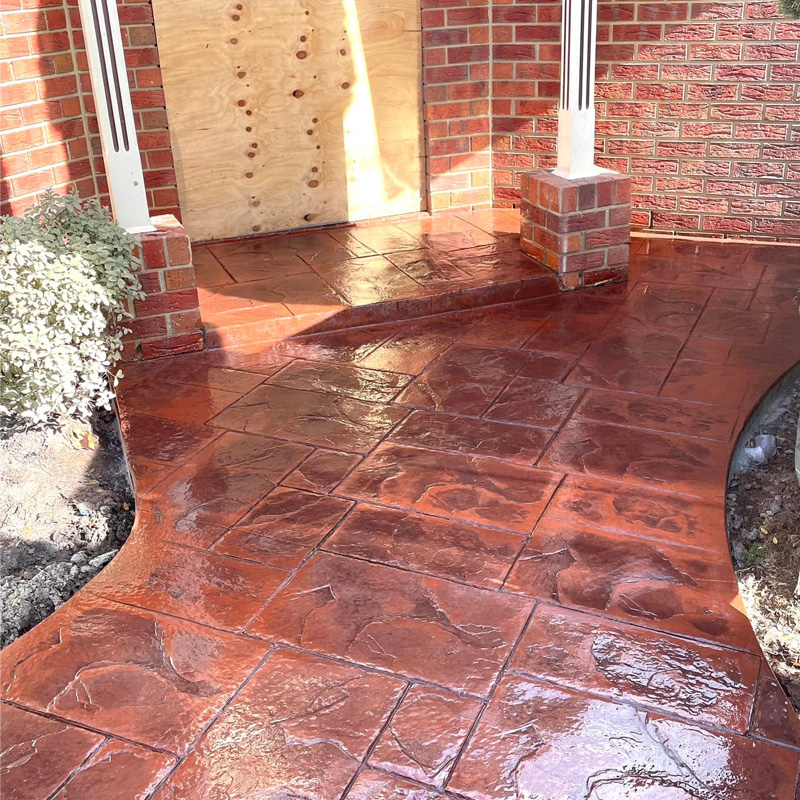 Glossy red stencilled concrete entry path at a brick home's front door