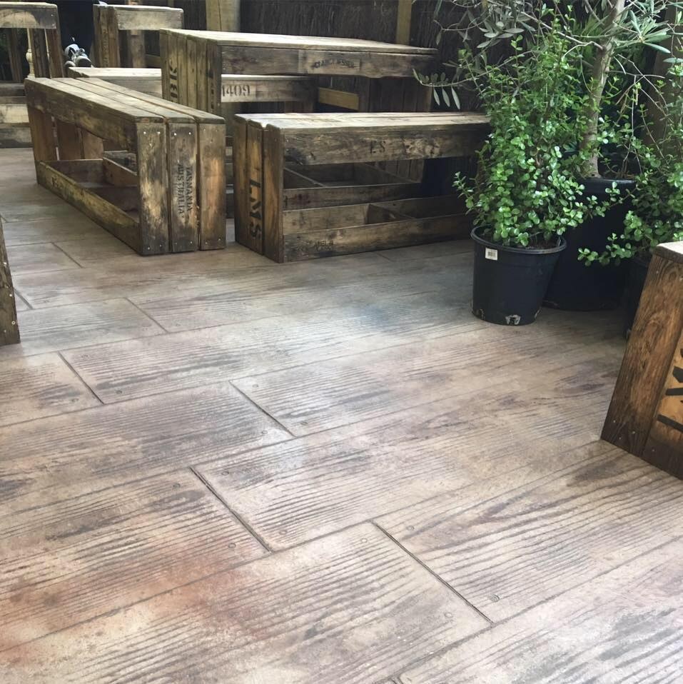 Timber-look stencilled concrete with outdoor timber tables and pot plants