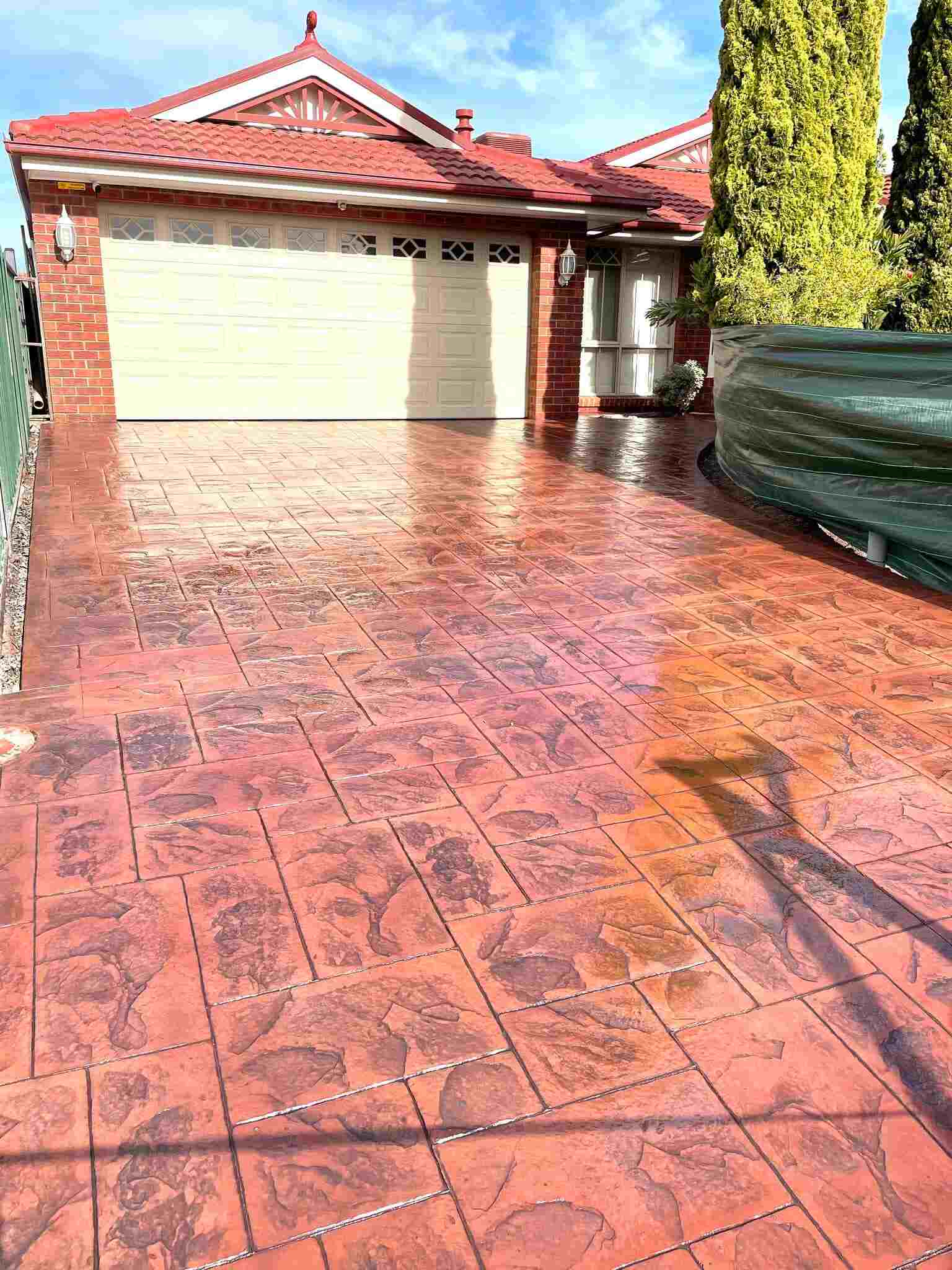 Glossy red stencilled concrete driveway leading to a double garage
