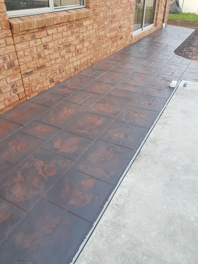 Dark stencilled concrete path beside a brick house and plain concrete