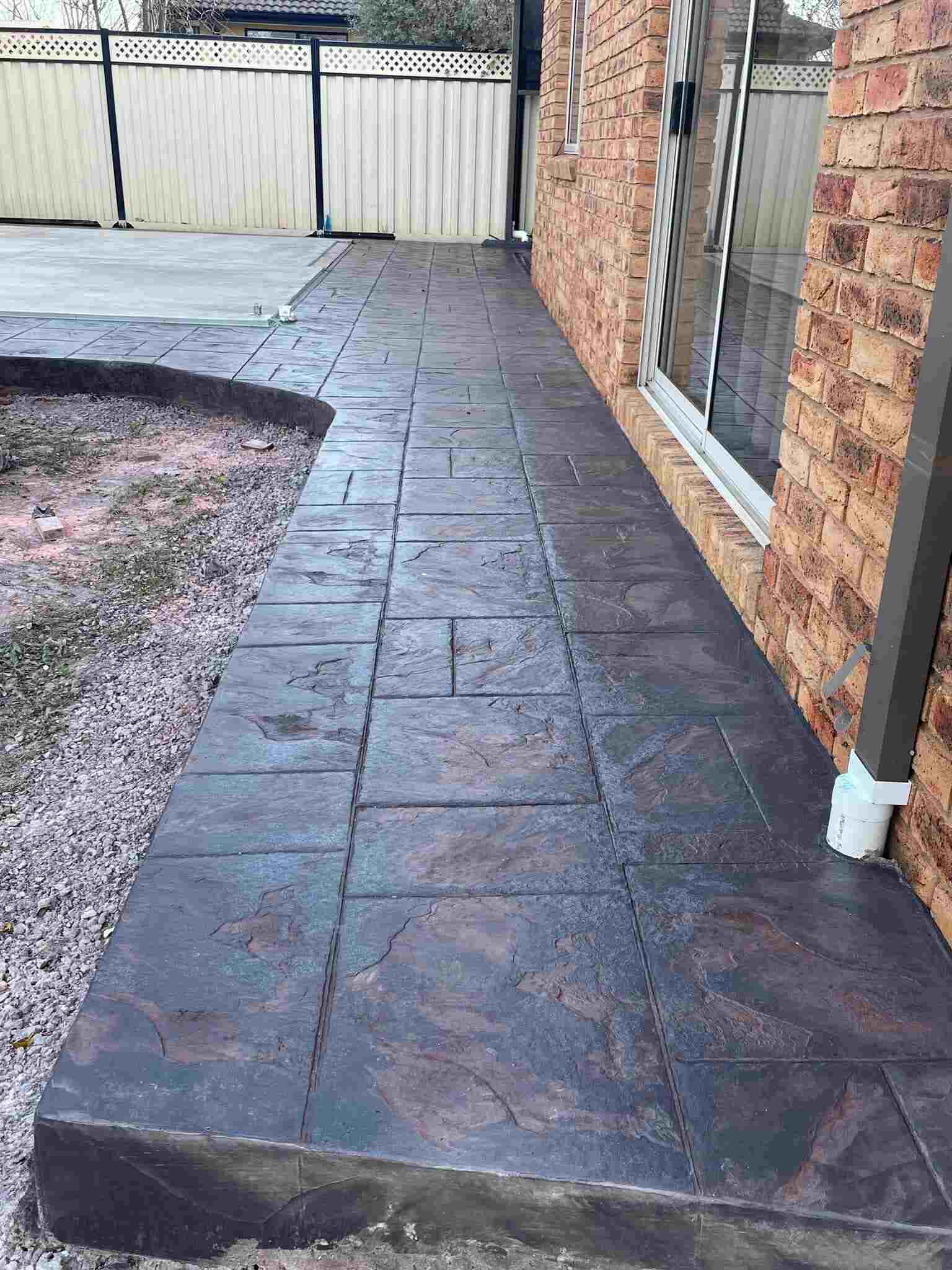 Grey stencilled concrete path along a brick house with a gravel garden