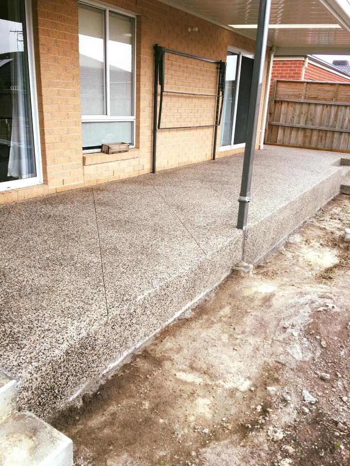 Exposed aggregate patio slab along the back of a brick house