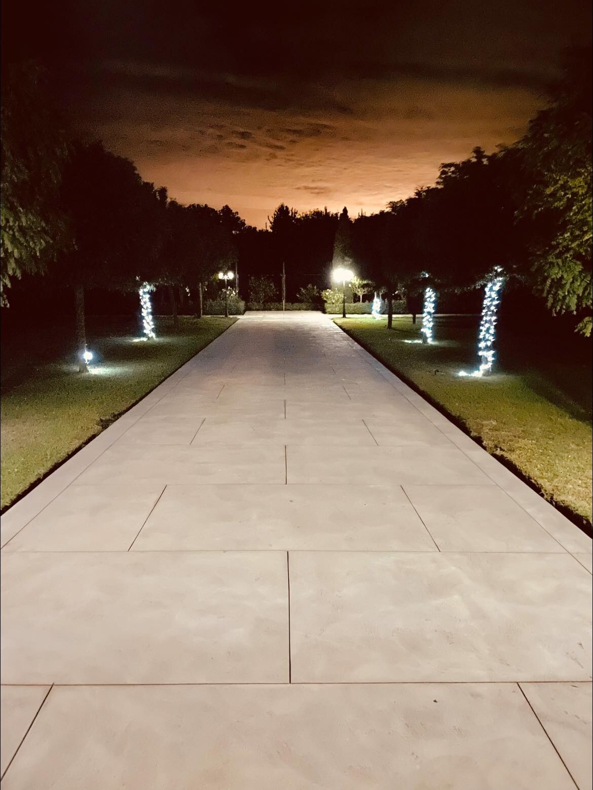 Long concrete driveway lit by garden lights at night