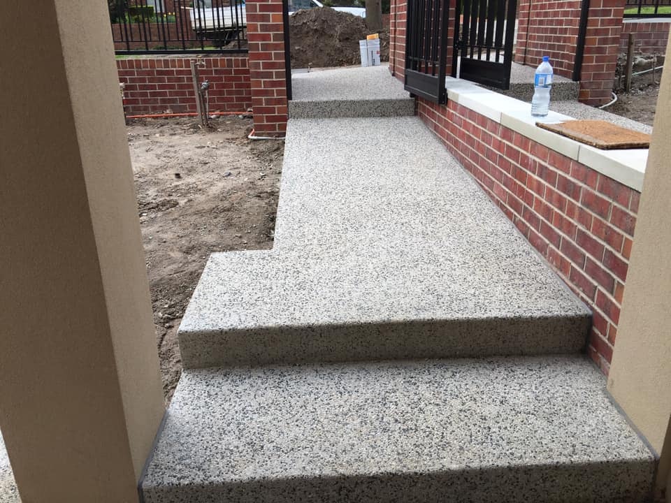 Light exposed aggregate path and steps beside a red brick wall