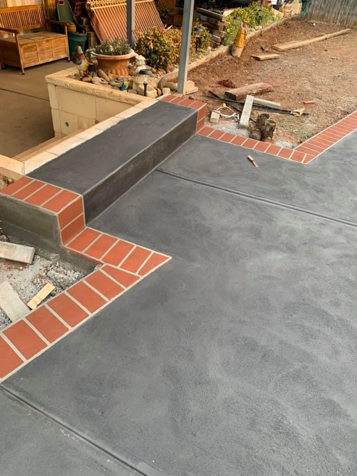 Grey concrete patio with a step and red brick paver edging